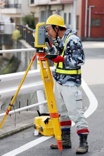 Licensed land surveyor using equipment to measure a property for a FEMA elevation certificate required for flood insurance and mortgage closings

