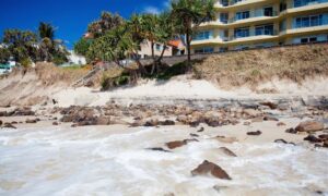 Eroded beachfront showing exposed roots and buildings near the shore, highlighting the need for a boundary survey after storm damage.