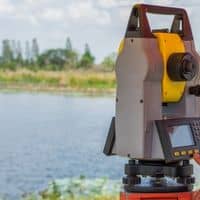 Licensed land surveyor using professional equipment to perform a boundary line survey near the shoreline