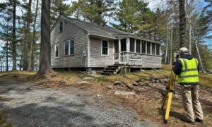 Surveyor measuring an older seasonal camp property in York, Maine before improvements