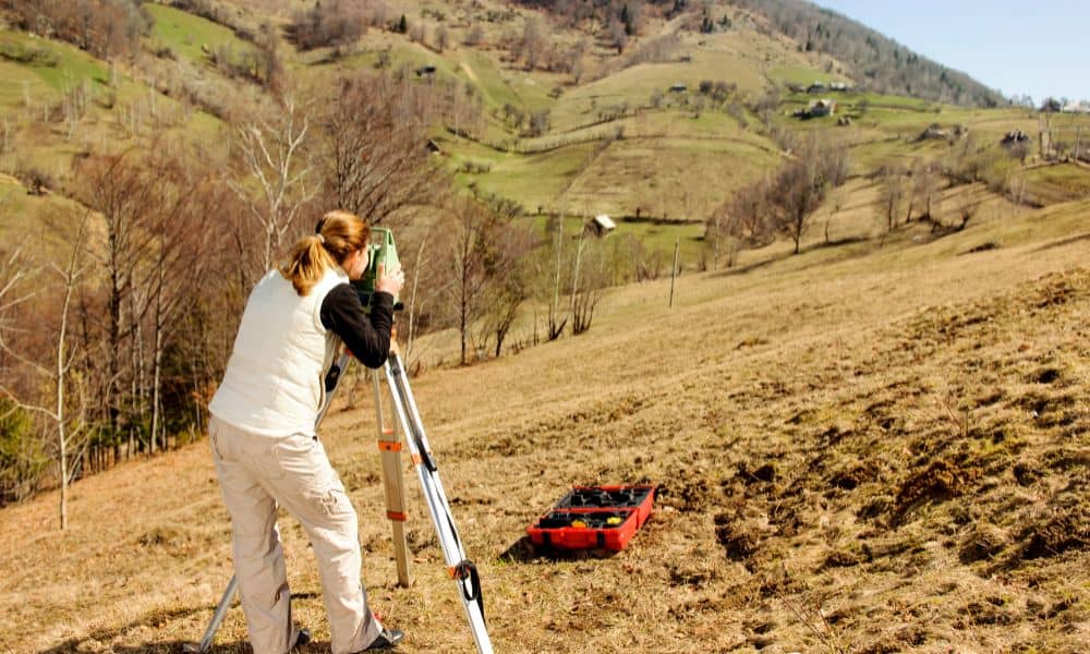 Land surveyor conducting a topographic survey on sloped rural terrain with visible elevation changes and survey tools, ideal for site planning in Maine.