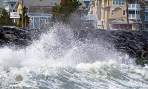High surf crashing against rocks near coastal homes, showing storm impacts that can affect FEMA elevation certificate requirements