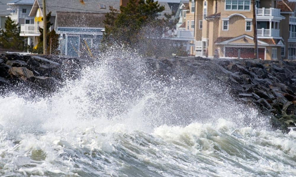 High surf crashing against rocks near coastal homes, showing storm impacts that can affect FEMA elevation certificate requirements