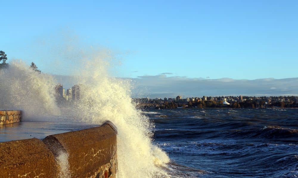 Waves crashing over a seawall during a coastal storm highlighting the need for a flood elevation survey for nearby homes