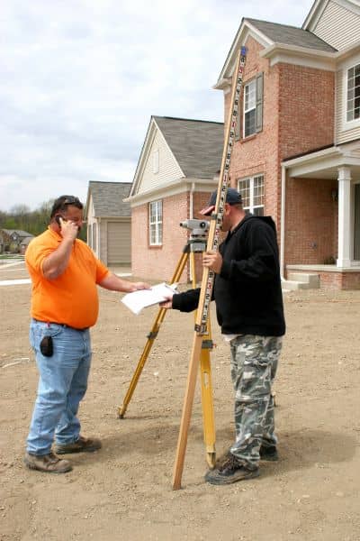  Licensed land surveyors checking property elevation to update FEMA elevation certificate after storm impacts
