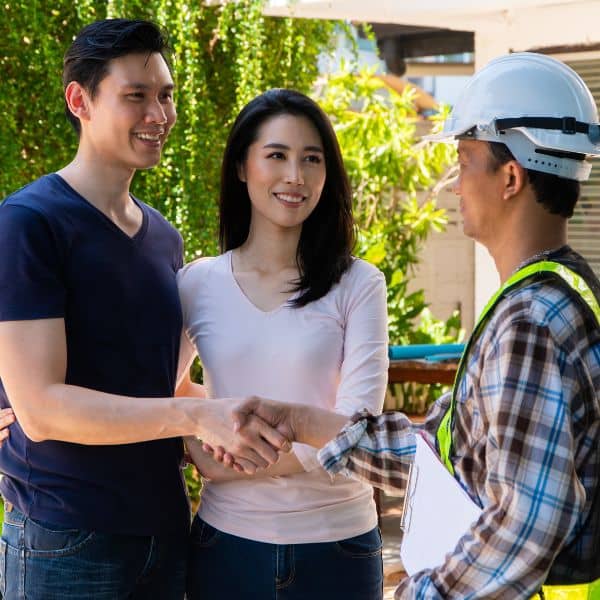 Smiling homeowners shaking hands with a land surveyor after receiving their elevation survey results confirming accurate flood risk
