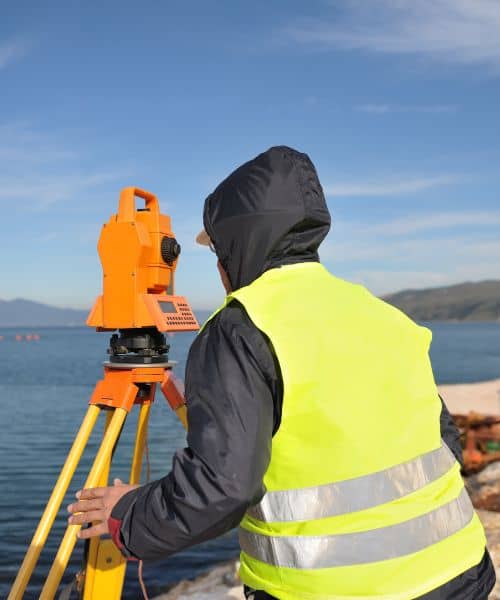 A surveyor using a total station near the coast to update measurements for a topographic survey